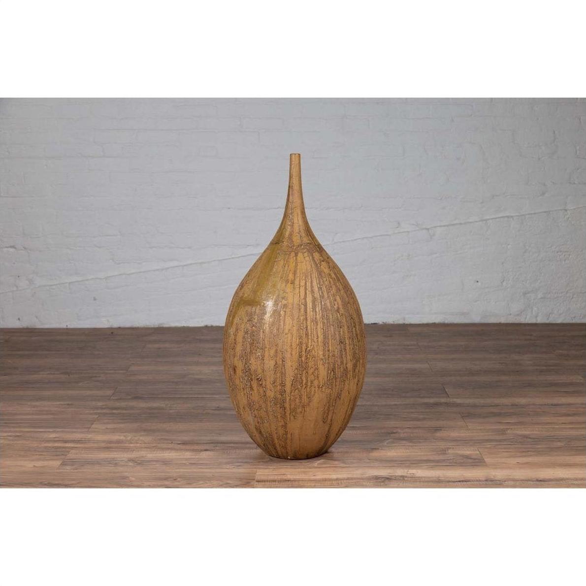 Mustard yellow ceramic vase with tapered spout on wooden floor against white brick wall indoors.