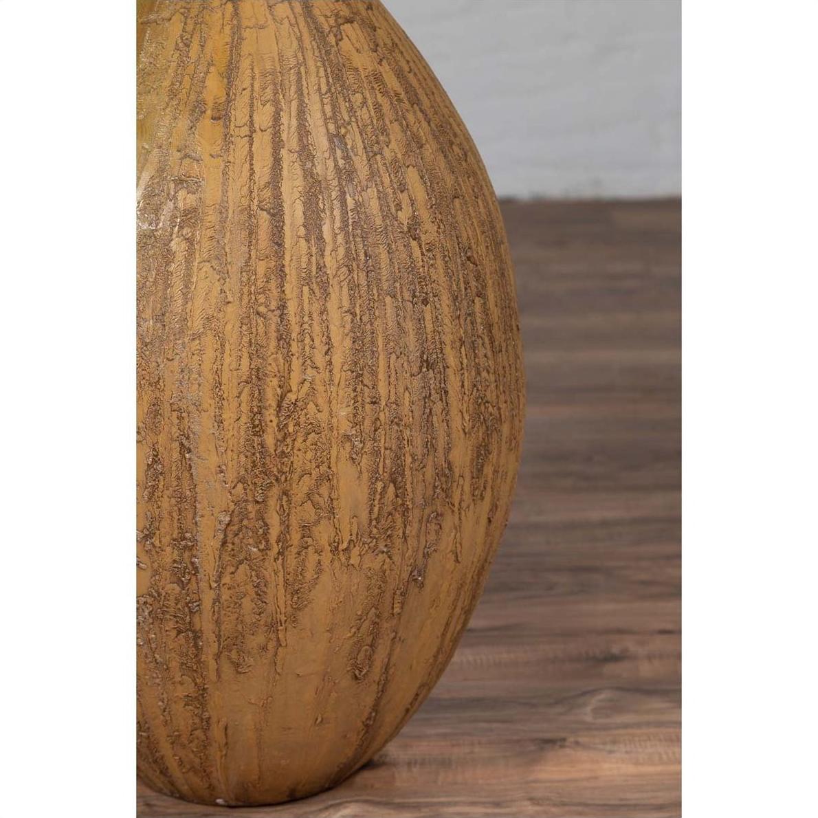 Mustard yellow ceramic vase with tapered spout on wooden floor against white wall, handmade Thai style.