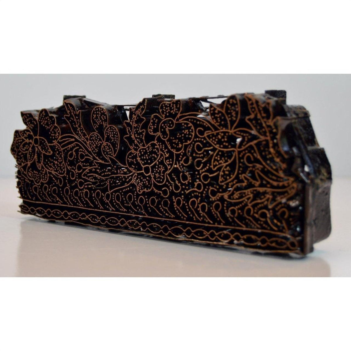 Close-up of copper batik ink block with intricate floral and leaf patterns, used for garment making.