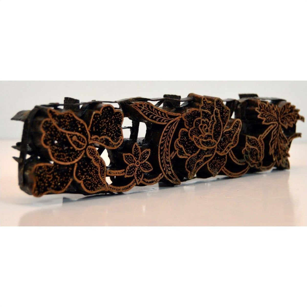 Close-up of a copper Batik ink block with carved black and gold floral patterns in an antique style.