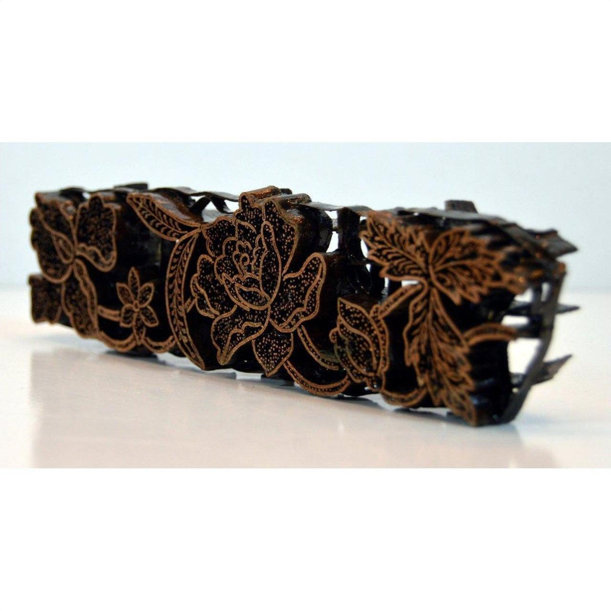 Close-up of a copper hair clip with batik ink block style and intricate gold floral patterns on a white surface.