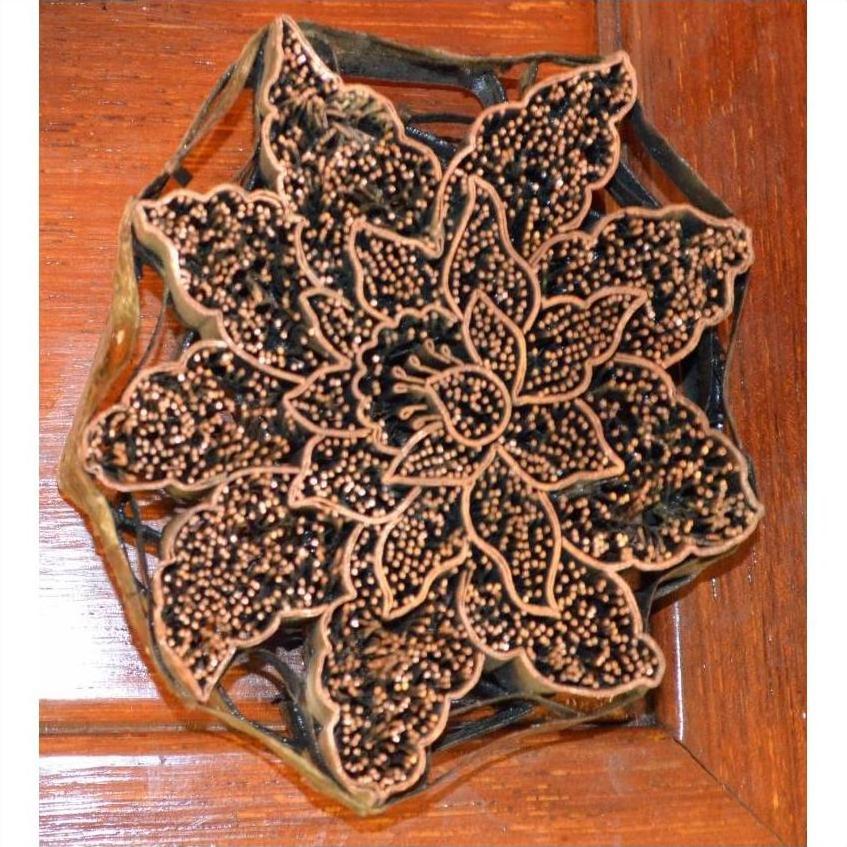 Close-up of a copper batik ink block with floral pattern on a wooden surface.