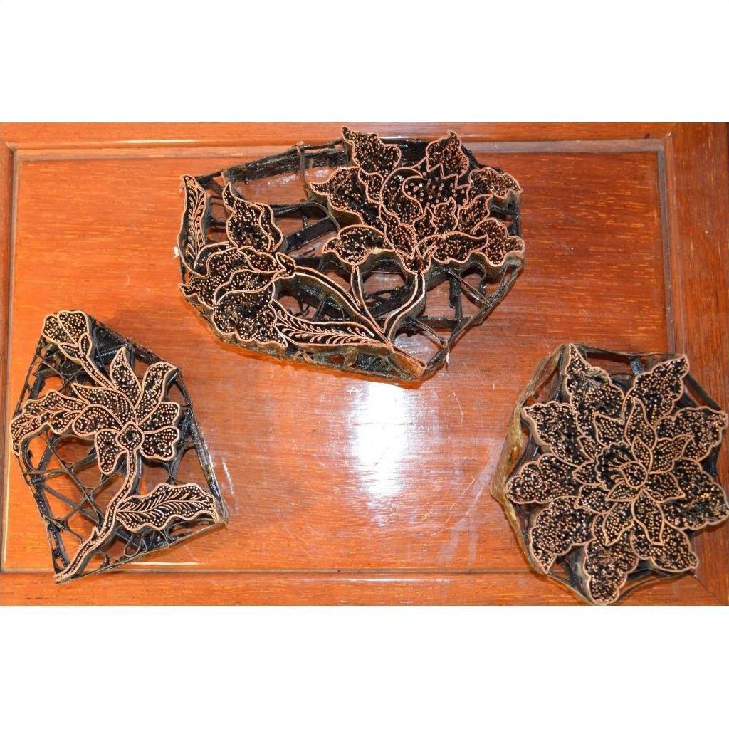 Copper Batik ink blocks with intricate floral designs for garment making on wooden surface, close-up view.