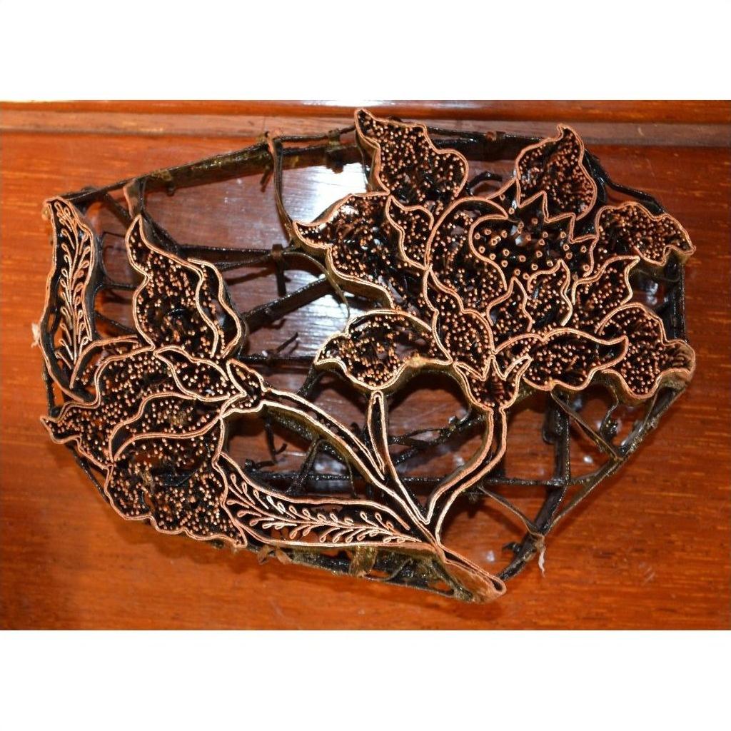 Close-up of copper Batik ink blocks with intricate floral designs on a wooden surface.