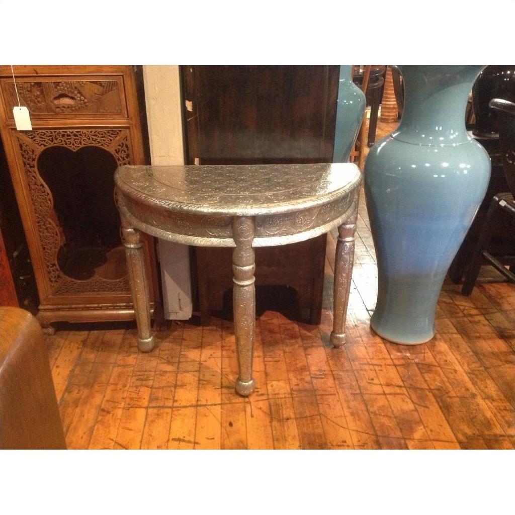 Silver nickel engraved demi-lune table next to a tall blue vase on a wooden floor.