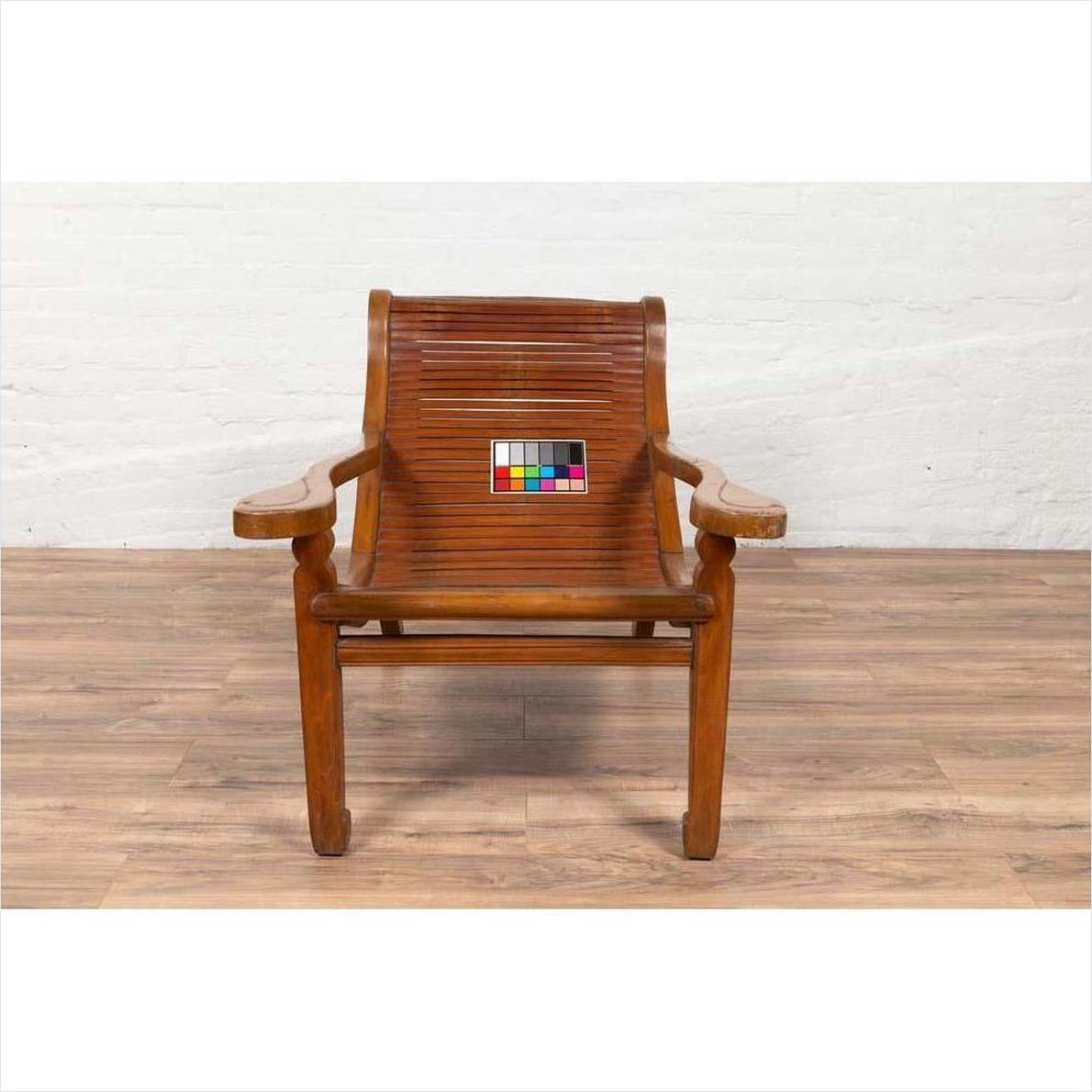 Brown wooden plantation lounge chair with curved slatted seat, color card on seat, on wood floor indoors.