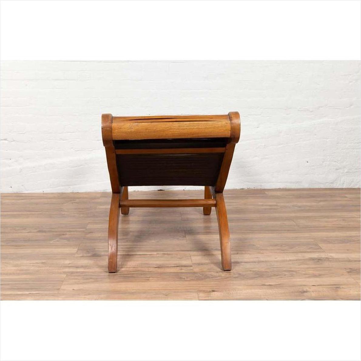 Brown wooden lounge chair with curved seat and slatted back, rear view on wooden floor indoors.