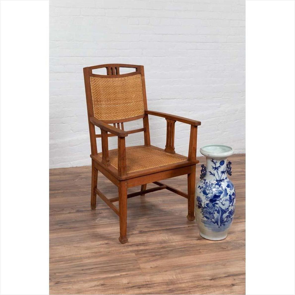 Brown Javanese teak armchair with rattan seat next to blue and white vase on wooden floor.