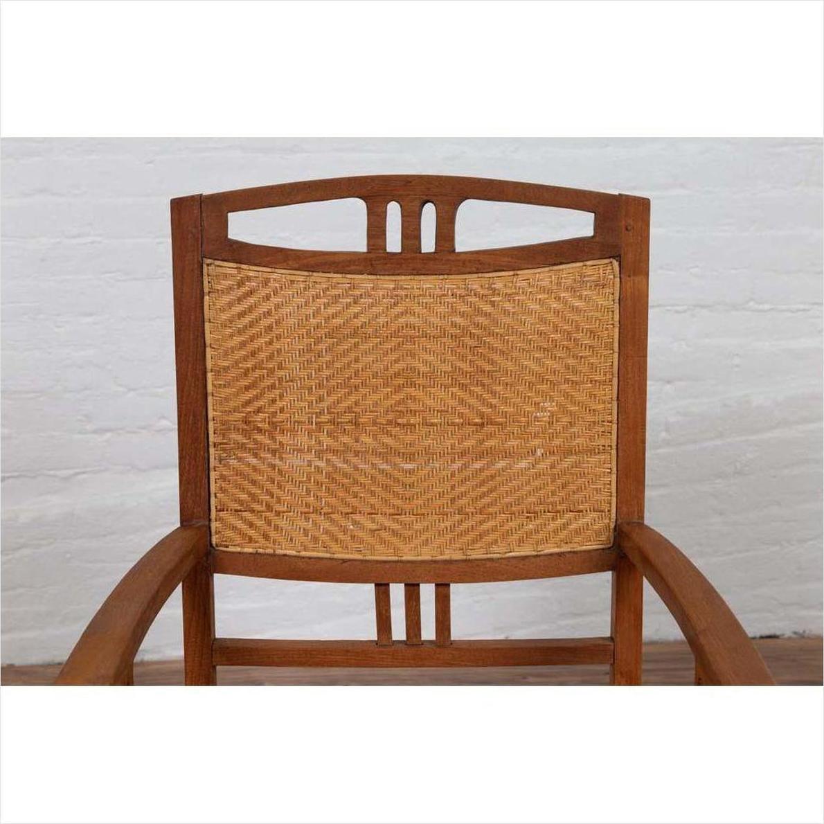 Brown teak and rattan Dutch Colonial Javanese armchair with triglyph motifs, against a white brick wall background.