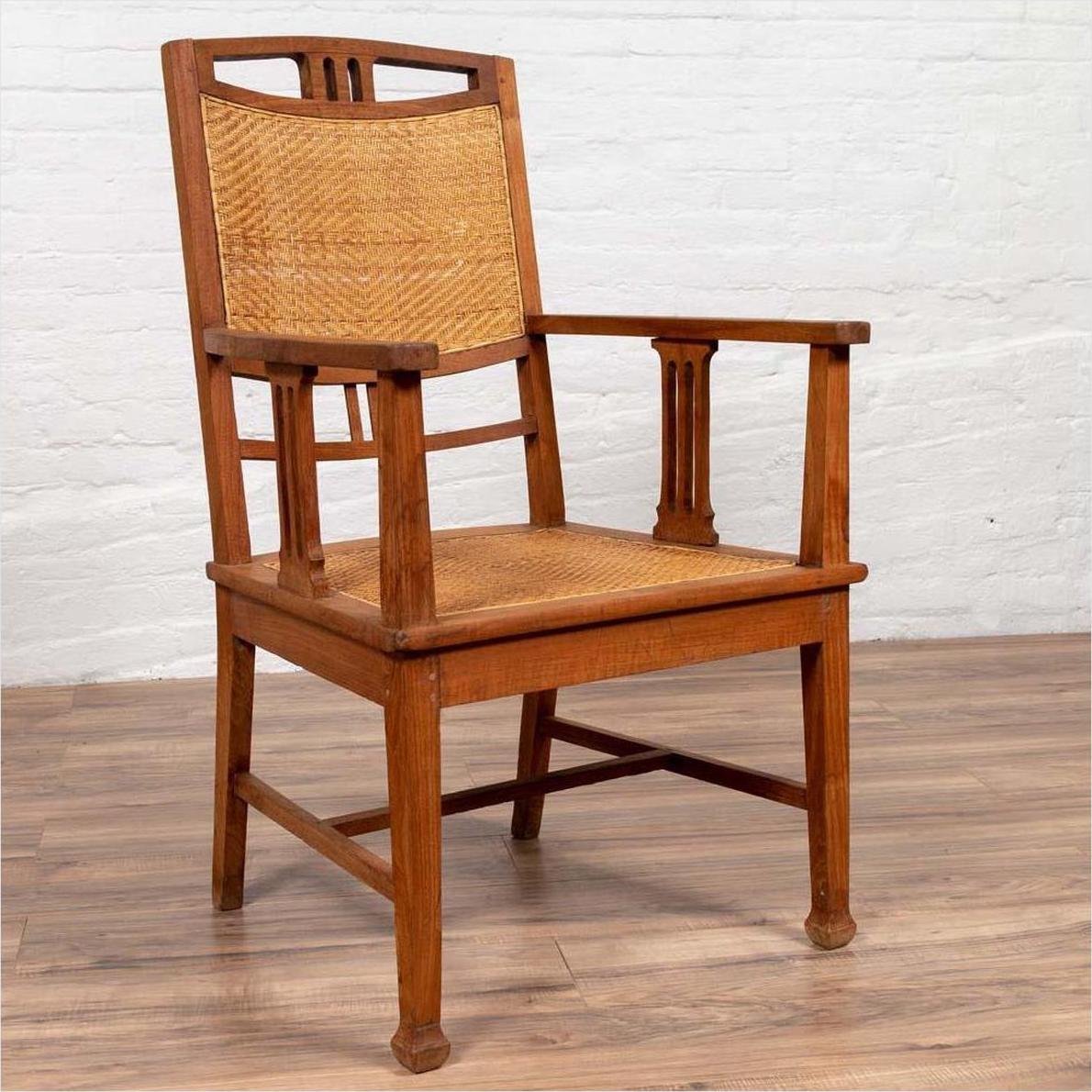 Brown teak and rattan Dutch Colonial Javanese armchair with triglyph motifs on wooden floor by a white brick wall.