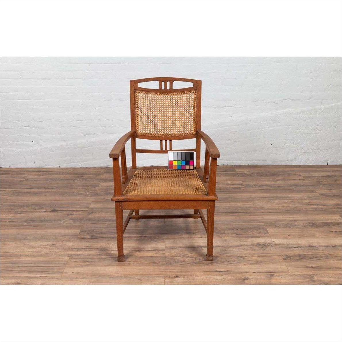 Brown teak and rattan Dutch Colonial Javanese armchair, color chart on seat, on wood floor against white brick wall.