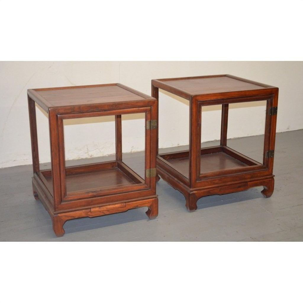 Two elmwood side tables with open sides and simple design on a gray floor against a white wall.
