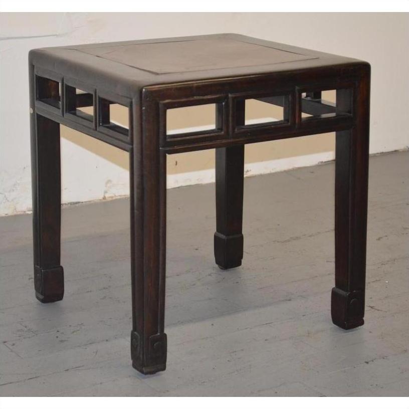 Brown elmwood stool with burl inlay and carved legs on a gray floor against a white wall.