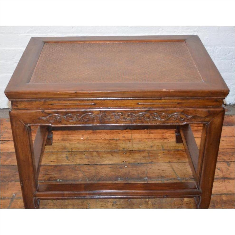 Brown elmwood stool or table with carved detailing, placed on wooden floor in front of a white brick wall.