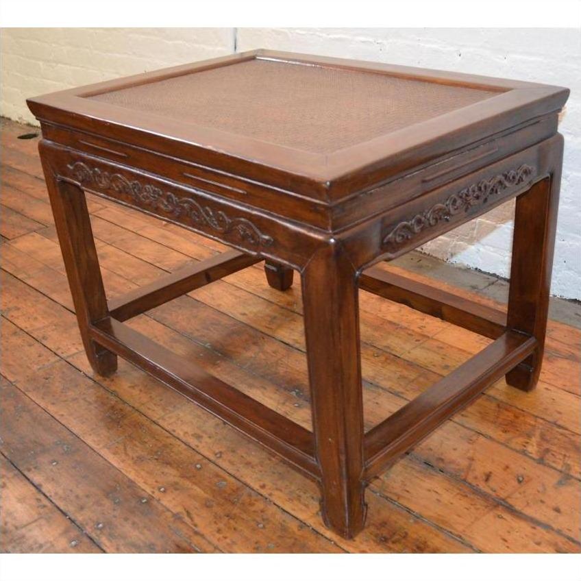Brown elmwood stool or table with carved floral details and straight legs on wooden floor beside white brick wall.