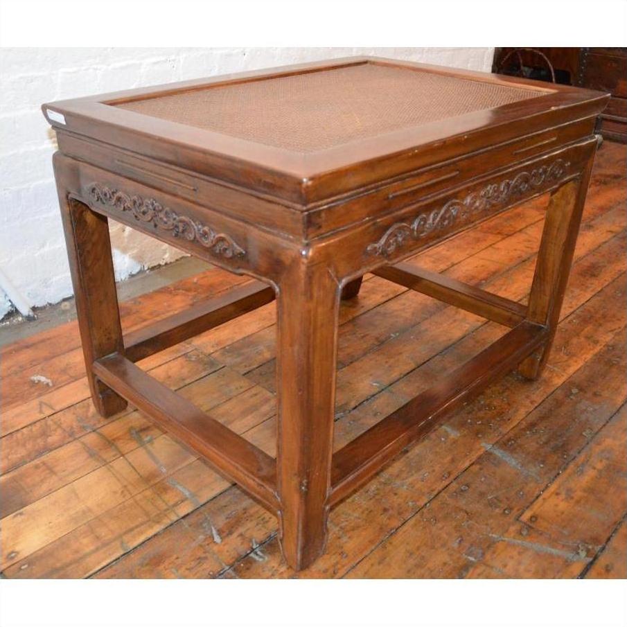 Brown wood Elmwood stool or table with carved sides, cane top, and sturdy legs on a wooden floor.
