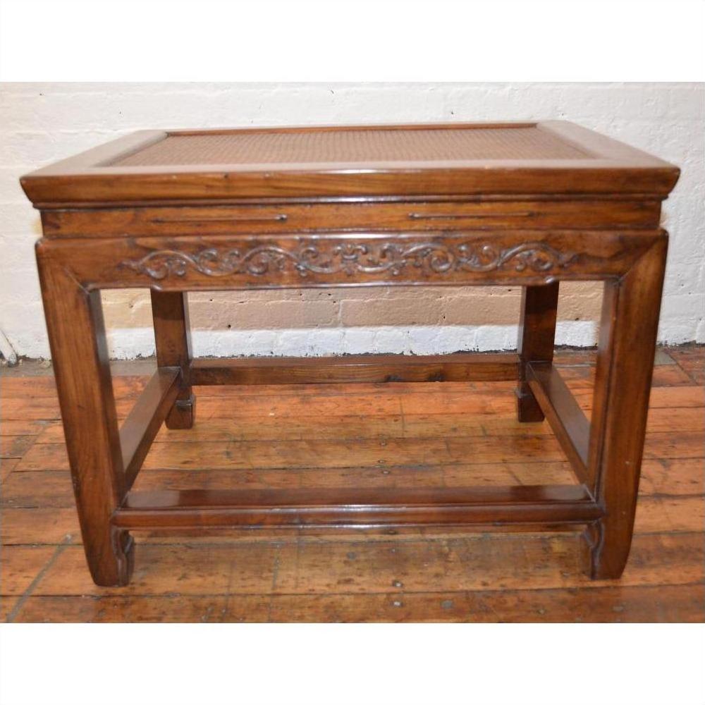 Brown elmwood stool or table with rattan inset top, carved scroll apron, and stretcher base on hardwood floor.