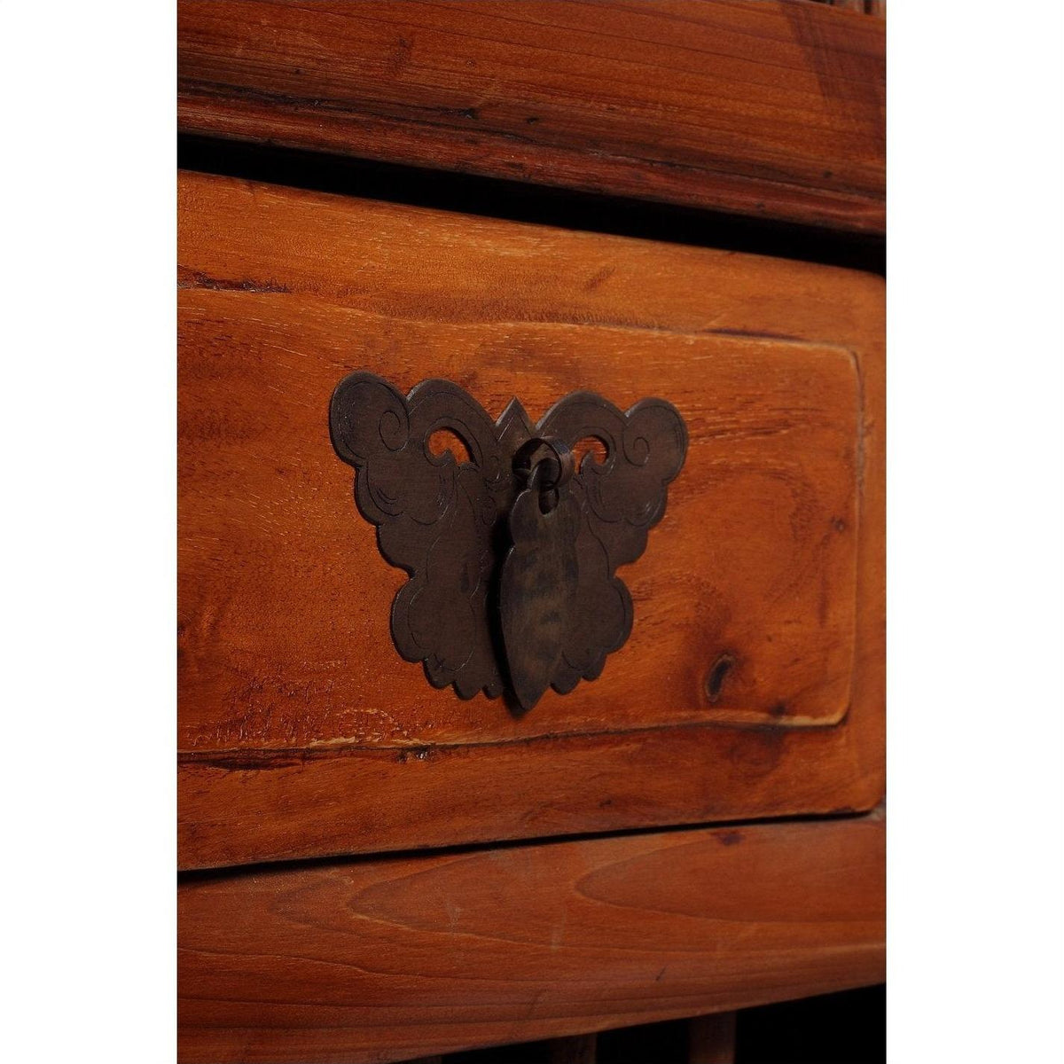 Close-up of dark wood fretwork and carved Chinese cabinet with ornate dark metal butterfly-shaped handle and keyhole.