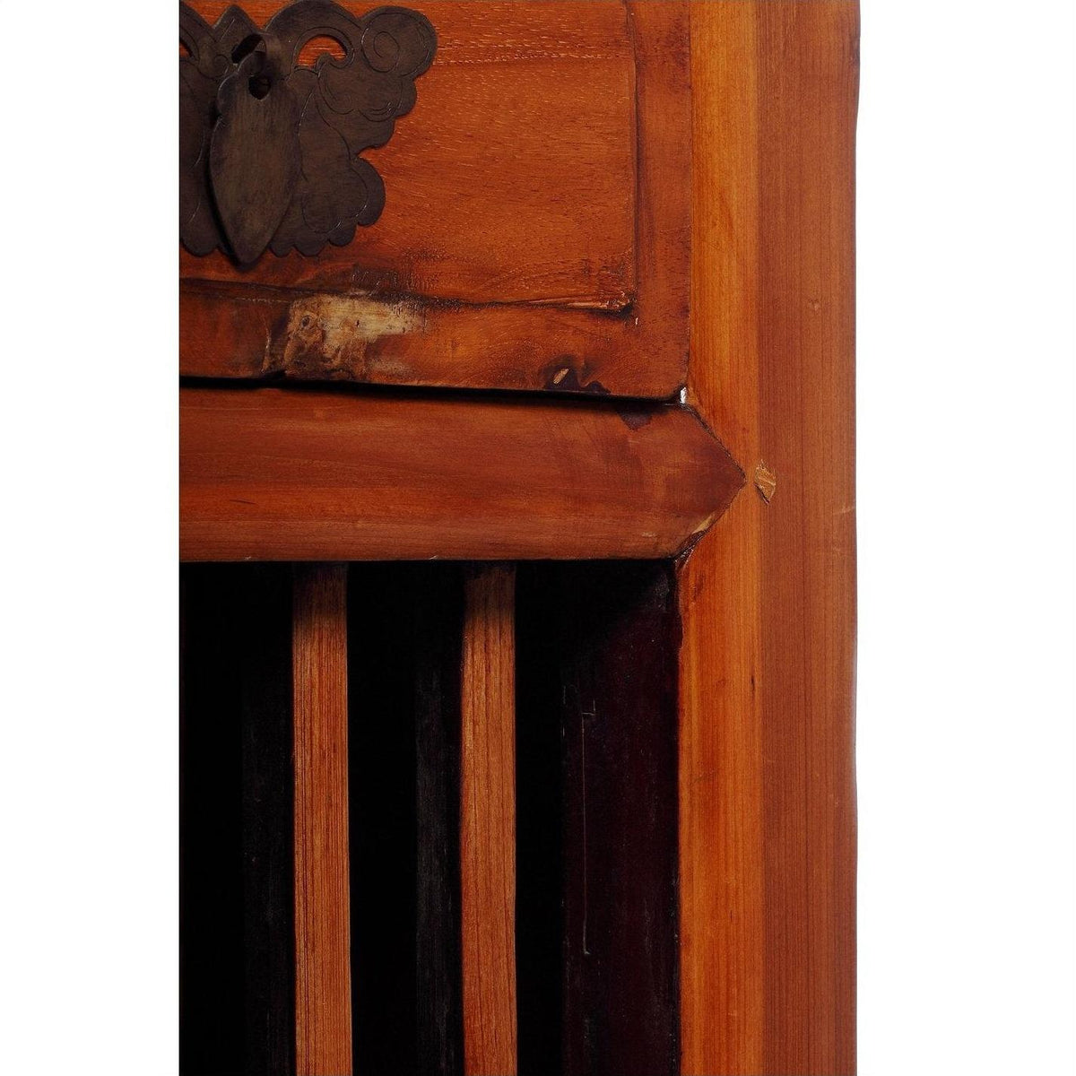 Close-up of a dark wood Chinese cabinet corner with carved fretwork, vertical slats, and butterfly metal hardware.