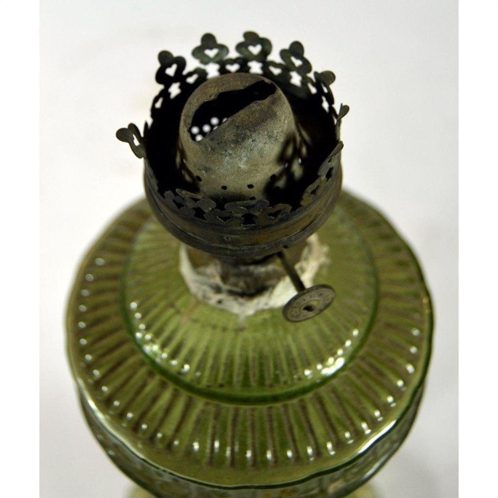 Close-up of a green glass oil lamp with decorative metal burner and exposed wick, in very good condition.