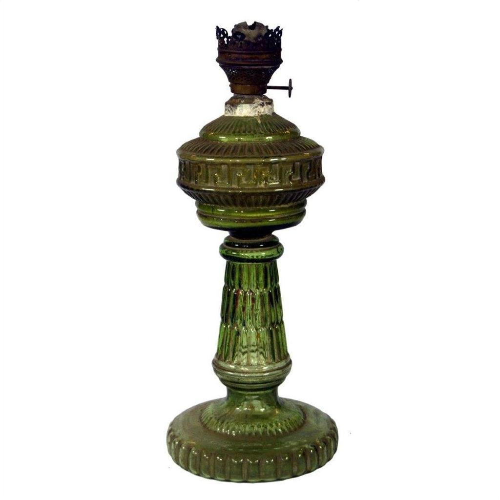 Close-up of antique green glass oil lamp with ornate embossed details, metal burner top, and ribbed pedestal.