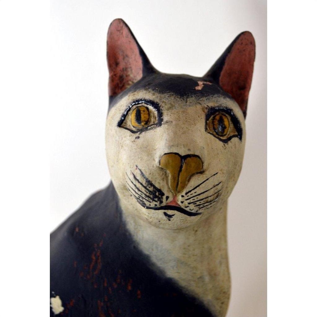 Close-up of hand carved black and white cat figurine with yellow eyes, detailed features, wood material visible.