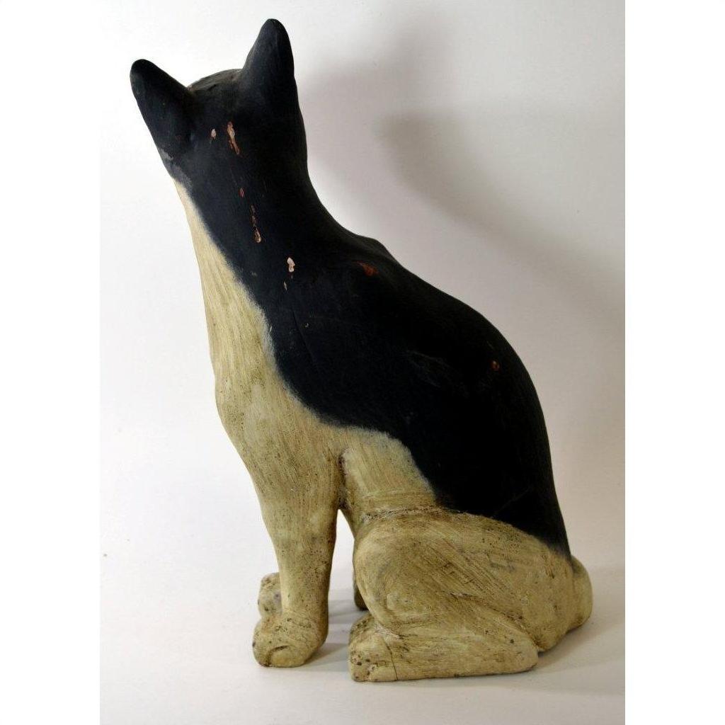 Rear view of a hand-carved cat statue with visible paint wear, wood material, on a white surface.