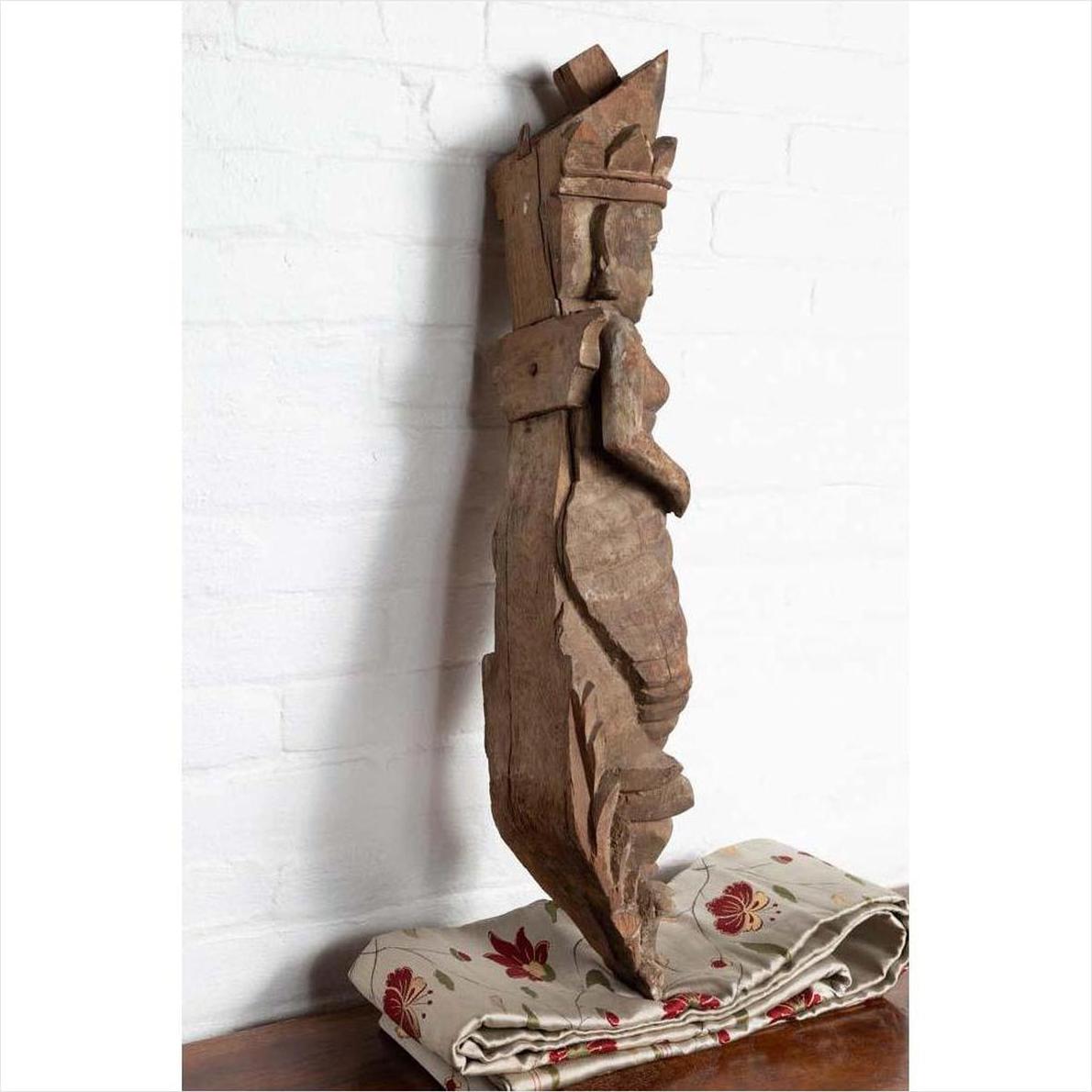 Hand carved brown stone Hindu deity statue on floral fabric in front of a white brick wall.