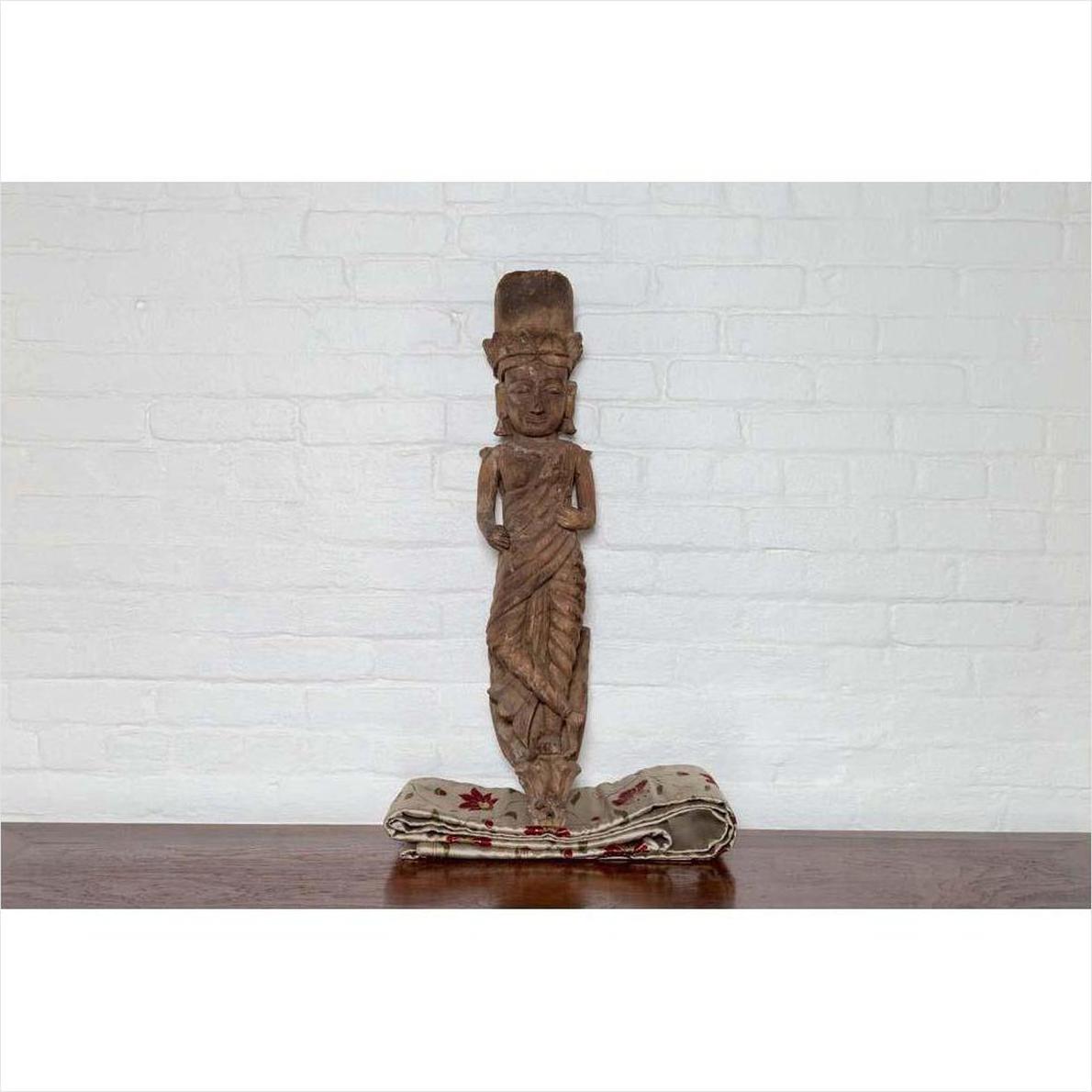 Brown wood statue of Hindu deity on patterned cloth, set against a white brick wall indoors.