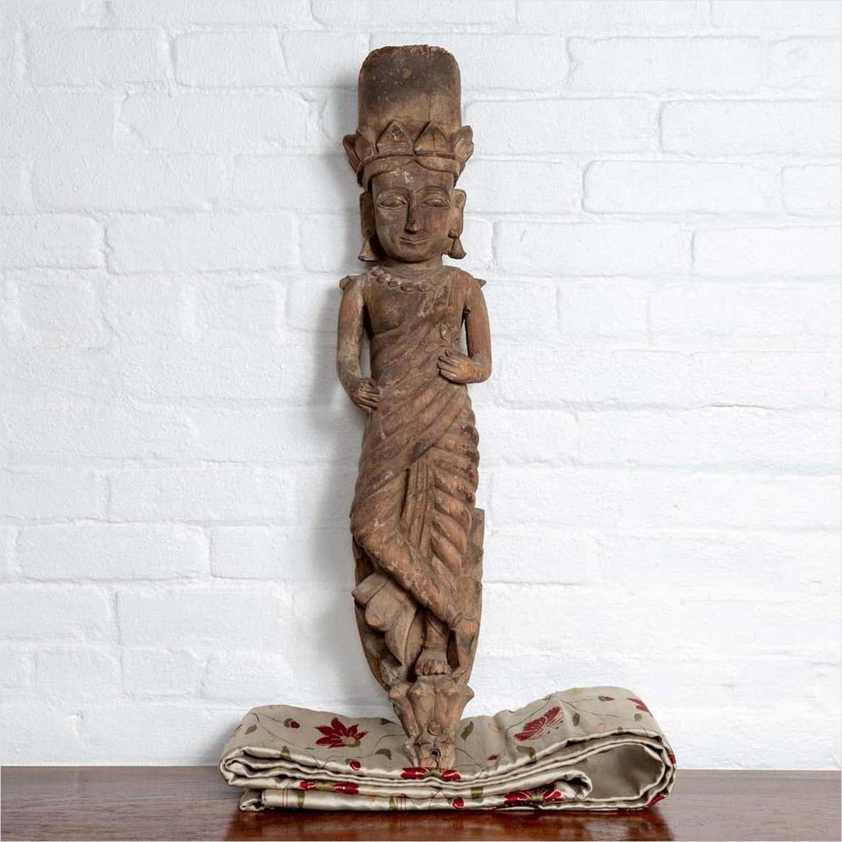 Brown hand-carved wood statue of Hindu deity with headdress on patterned fabric.