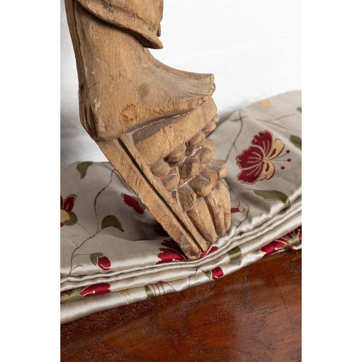 Brown wood mother and child statue on floral fabric, Indian style carving, indoor setting.