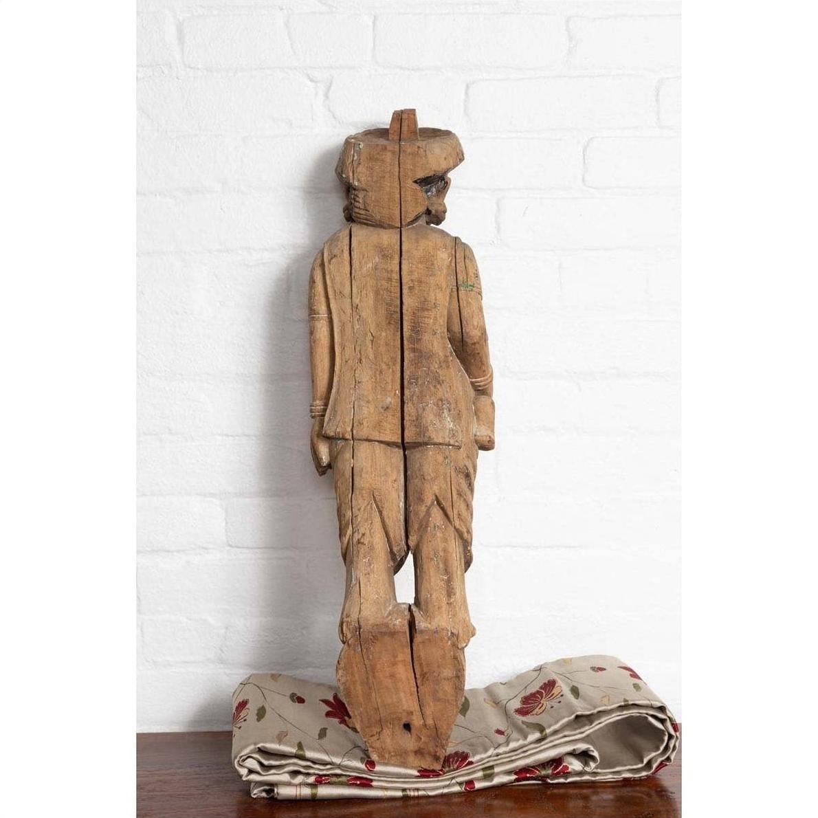 Brown hand-carved wood statue of mother and child on patterned cloth, white brick wall background.