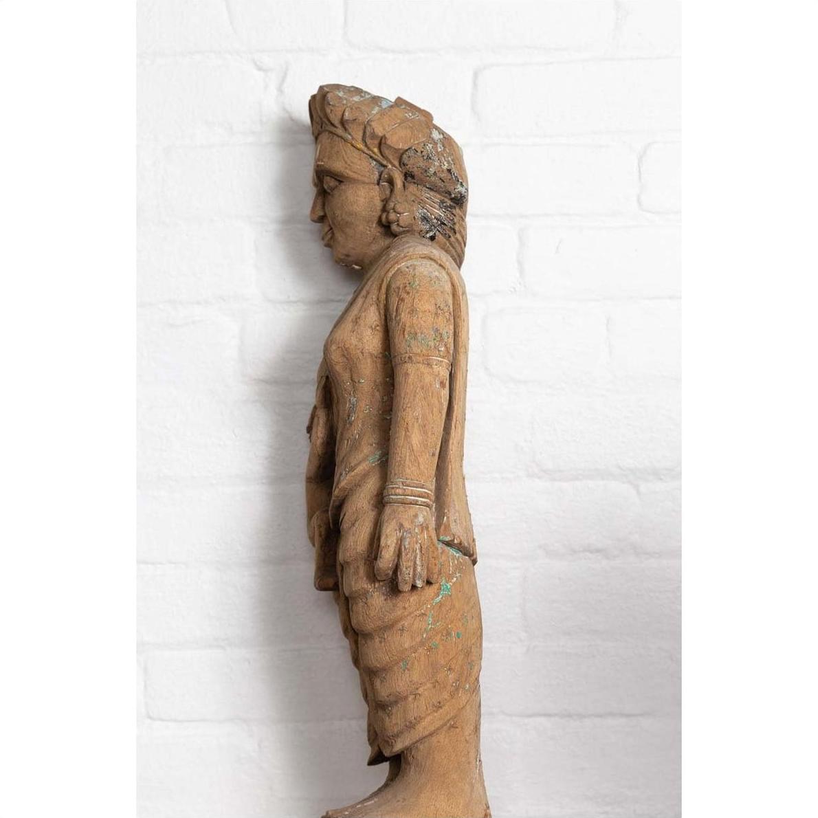 Brown hand carved wood mother and child statue from Gujarat, side view, beside white brick wall.