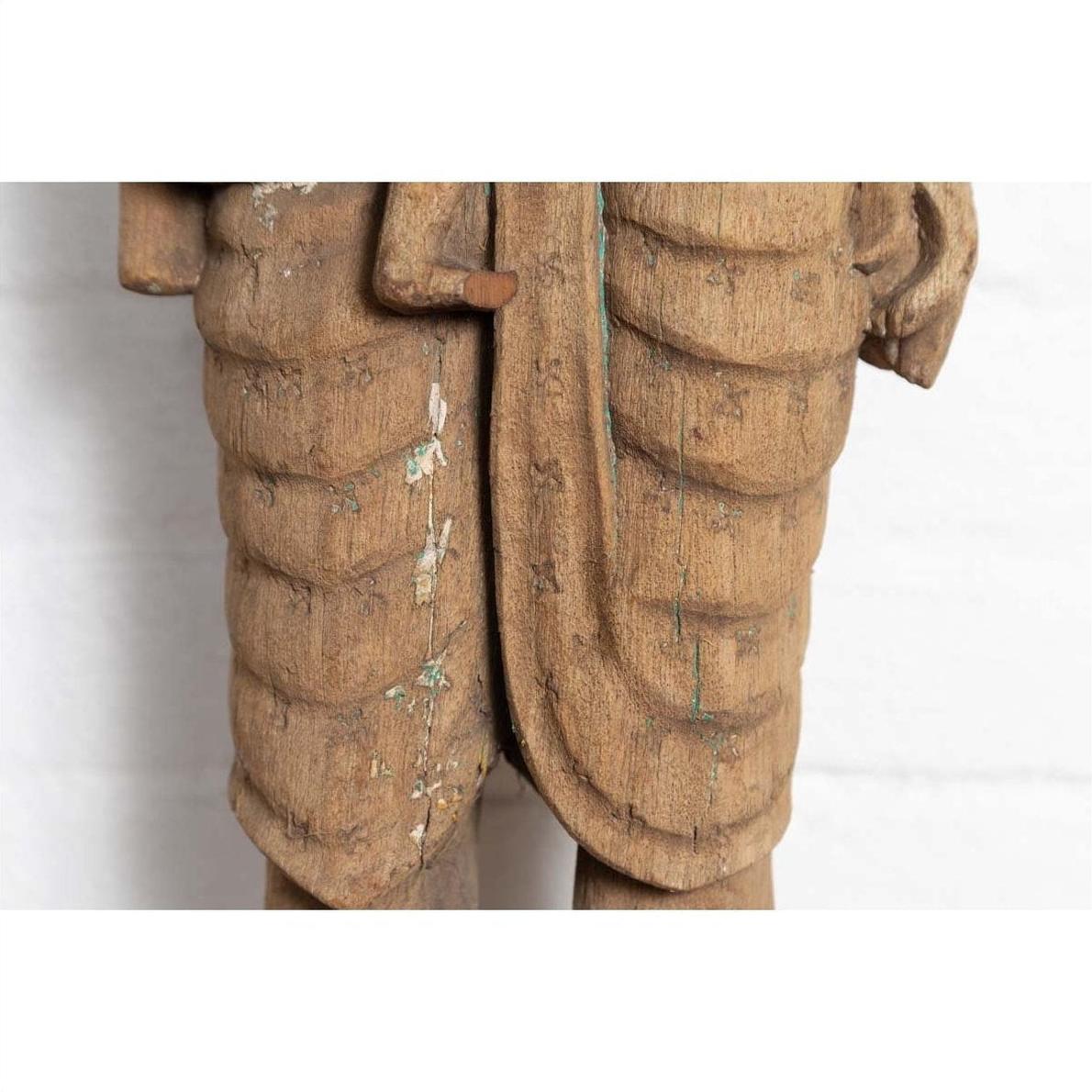 Close-up of brown carved wood statue from Gujarat showing mother and child with ribbed texture.