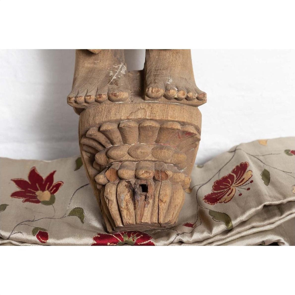 Close-up of brown carved wooden feet on Indian temple statue from Gujarat, mother and child motif.