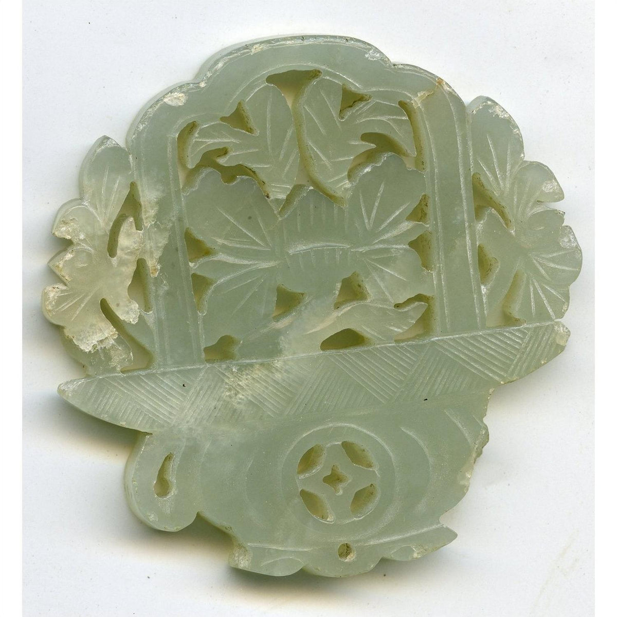 Close-up of pale green jade medallion with hand-carved floral and leaf patterns, 2"x2"x1/4", intricate cut-outs.
