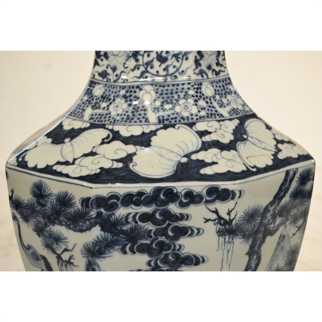 Blue and white porcelain vase with hand painted tree, cloud, and butterfly designs on a square base.