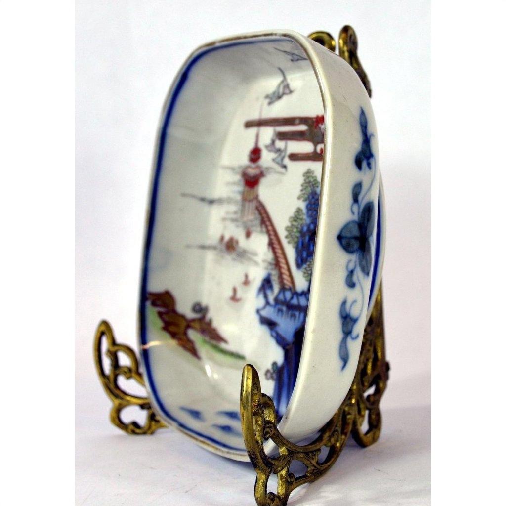 Close-up of blue and red hand painted Imari porcelain bowl on ornate gold metal stand, Asian-style landscape design.