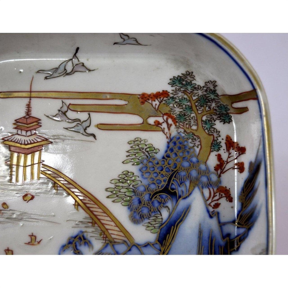 Close-up of hand painted Imari porcelain bowl with trees, birds, and pagoda by bridge design; minor casting marks visible.