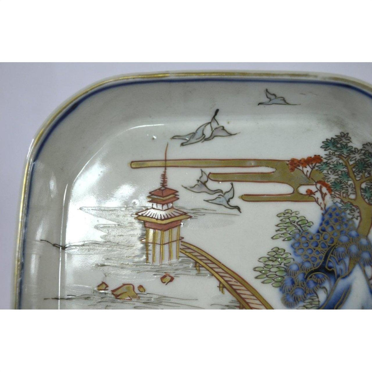 Blue and white porcelain Imari bowl with hand painted landscape featuring pagoda, birds, trees, bridge.