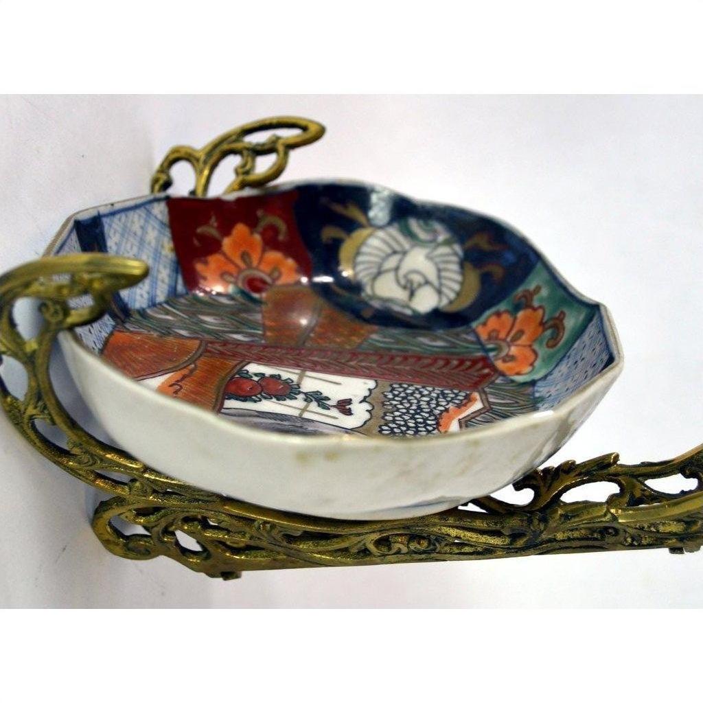 Colorful hand painted Imari porcelain plate with floral patterns on a gold-toned metal stand, close-up view.