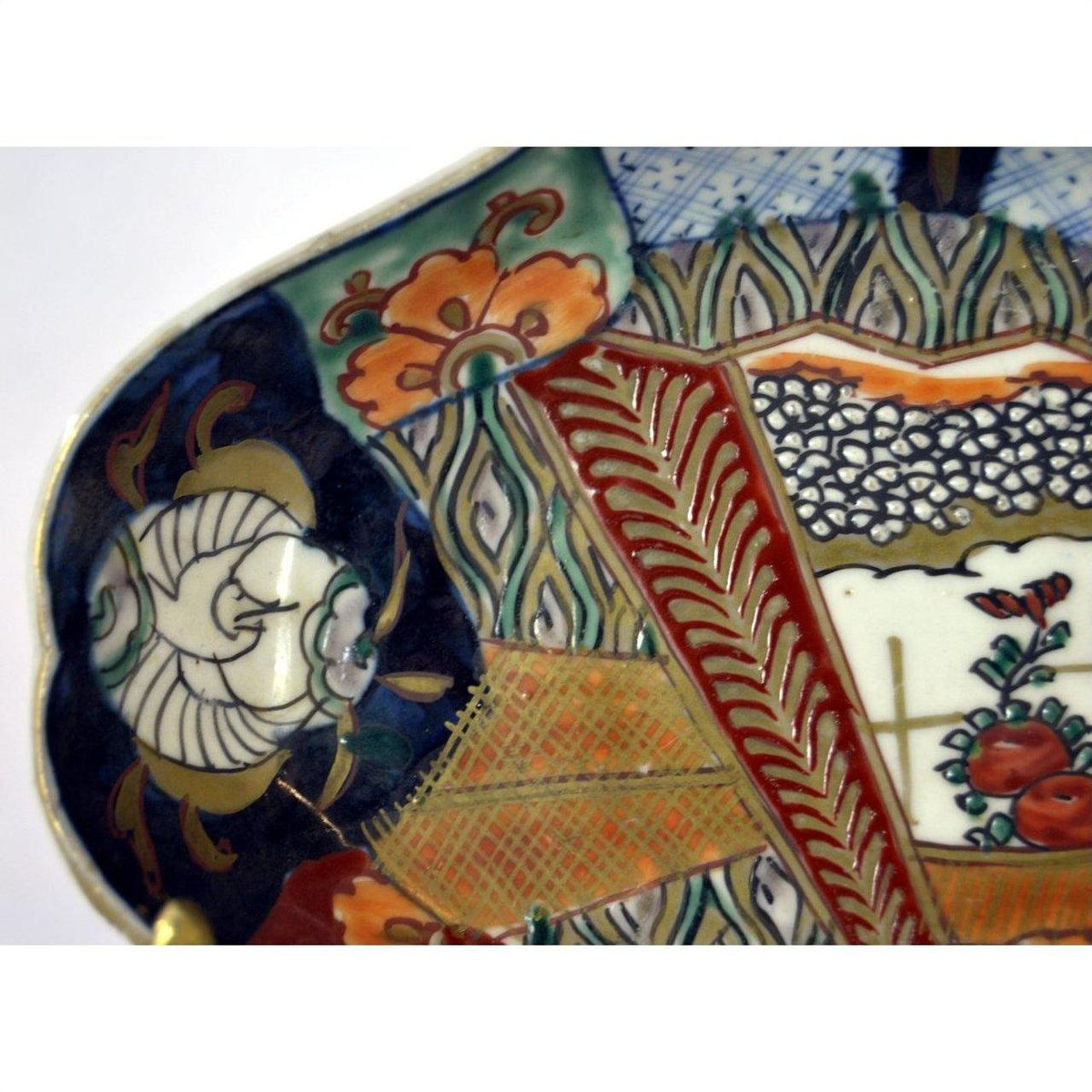 Close-up of red, blue, gold, and green hand painted Imari ceramic plate with floral and geometric patterns.