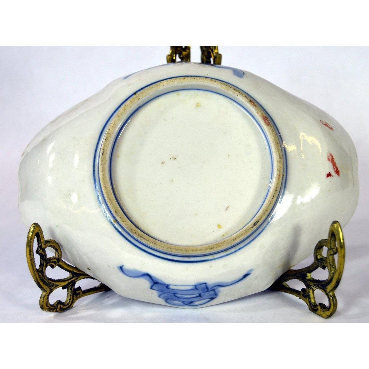 Blue and white ceramic plate on ornate metal stand, neutral background, indoor setting.