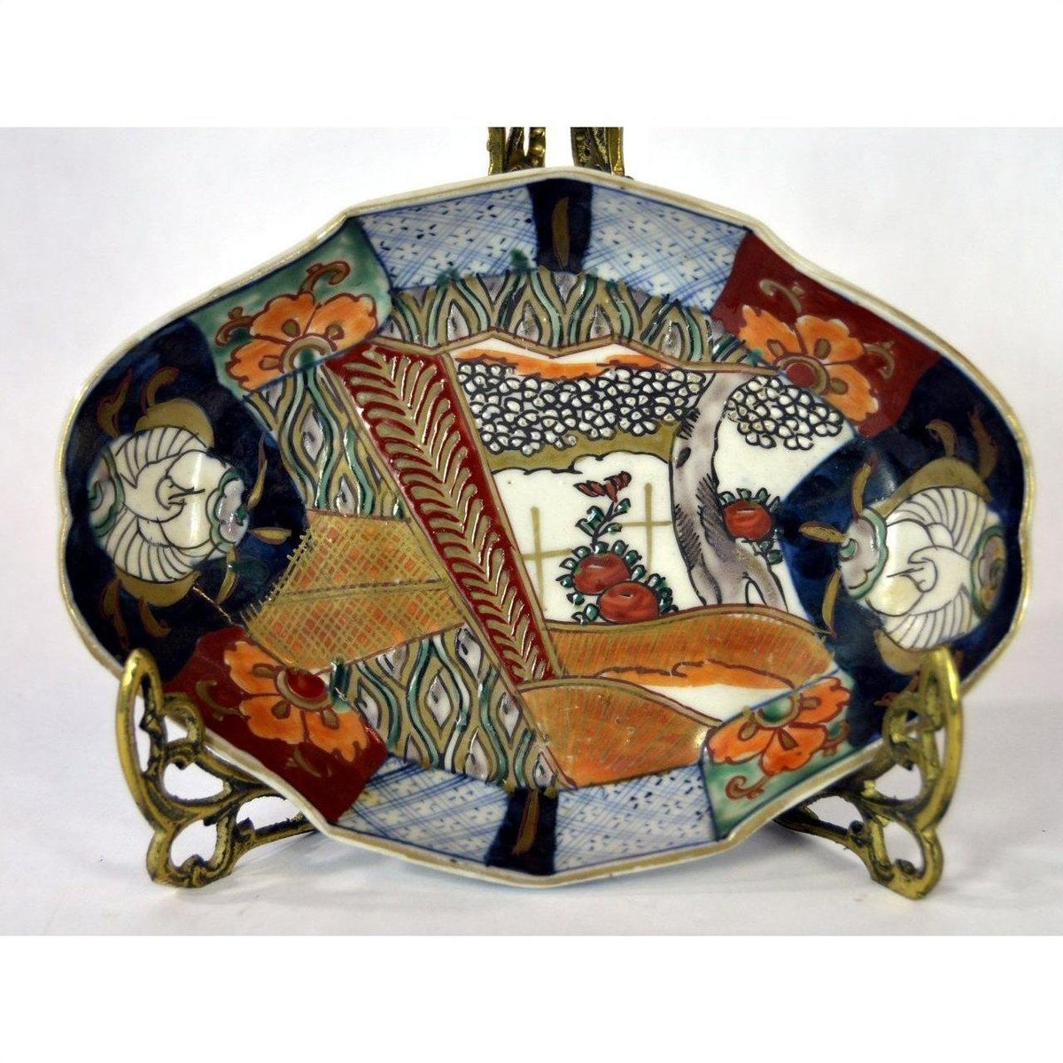 Colorful hand painted ceramic Imari plate with floral and geometric patterns on a decorative brass stand.