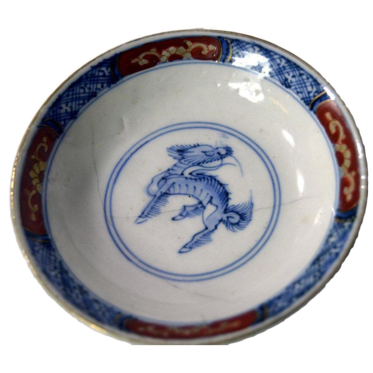 Blue, red, and gold ceramic plate with blue mythical creature pattern, shown on white background.