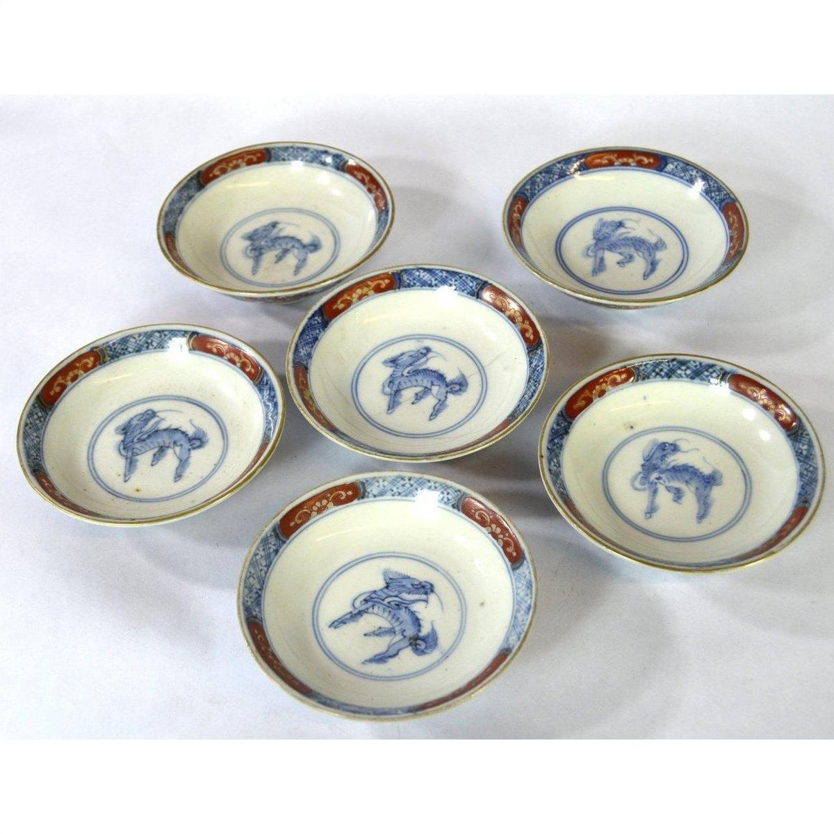 Set of six blue and white hand painted Imari porcelain small plates with animal designs and decorative borders on table.