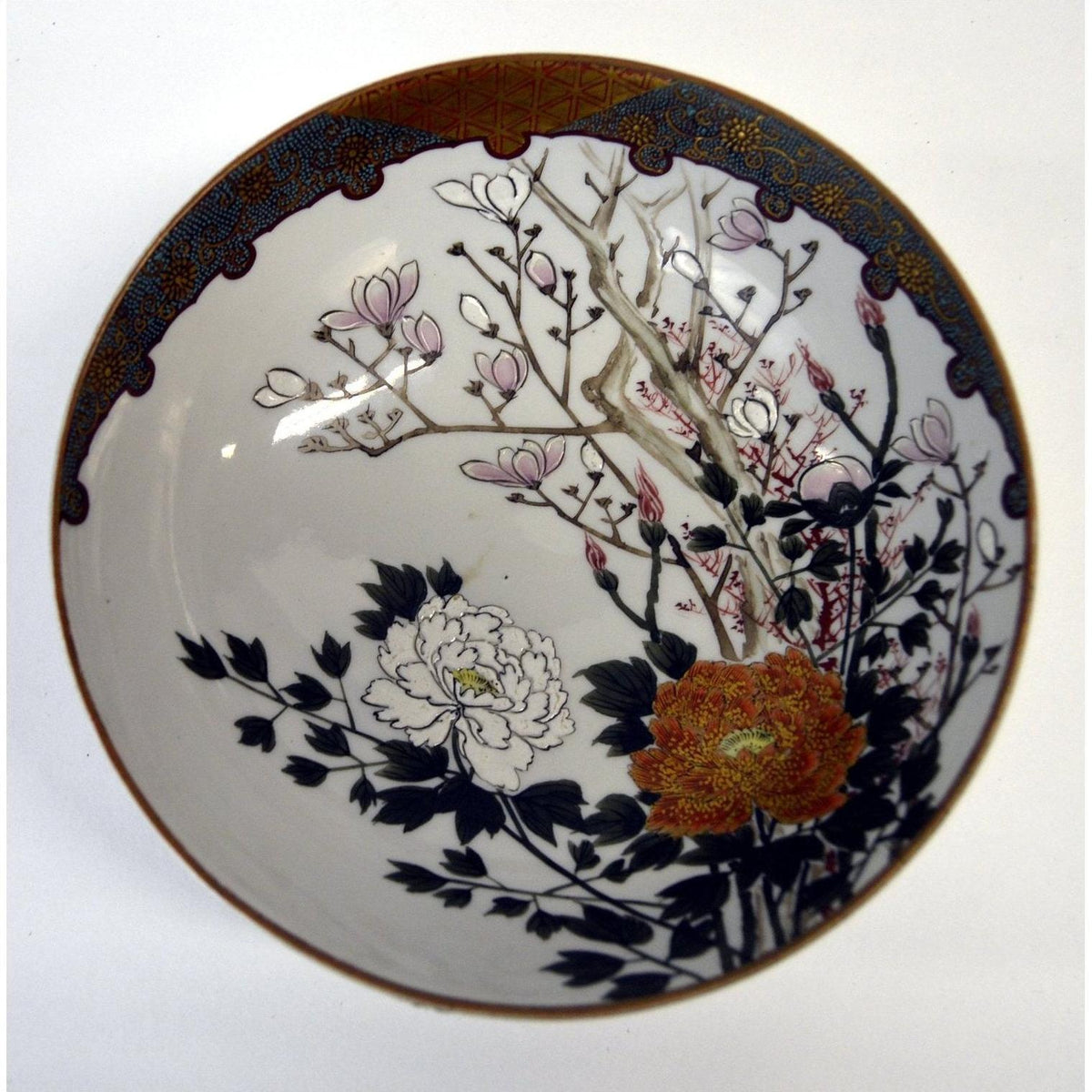 White porcelain Kutani bowl with hand painted pink, orange, and white floral designs on dark branches, close-up.