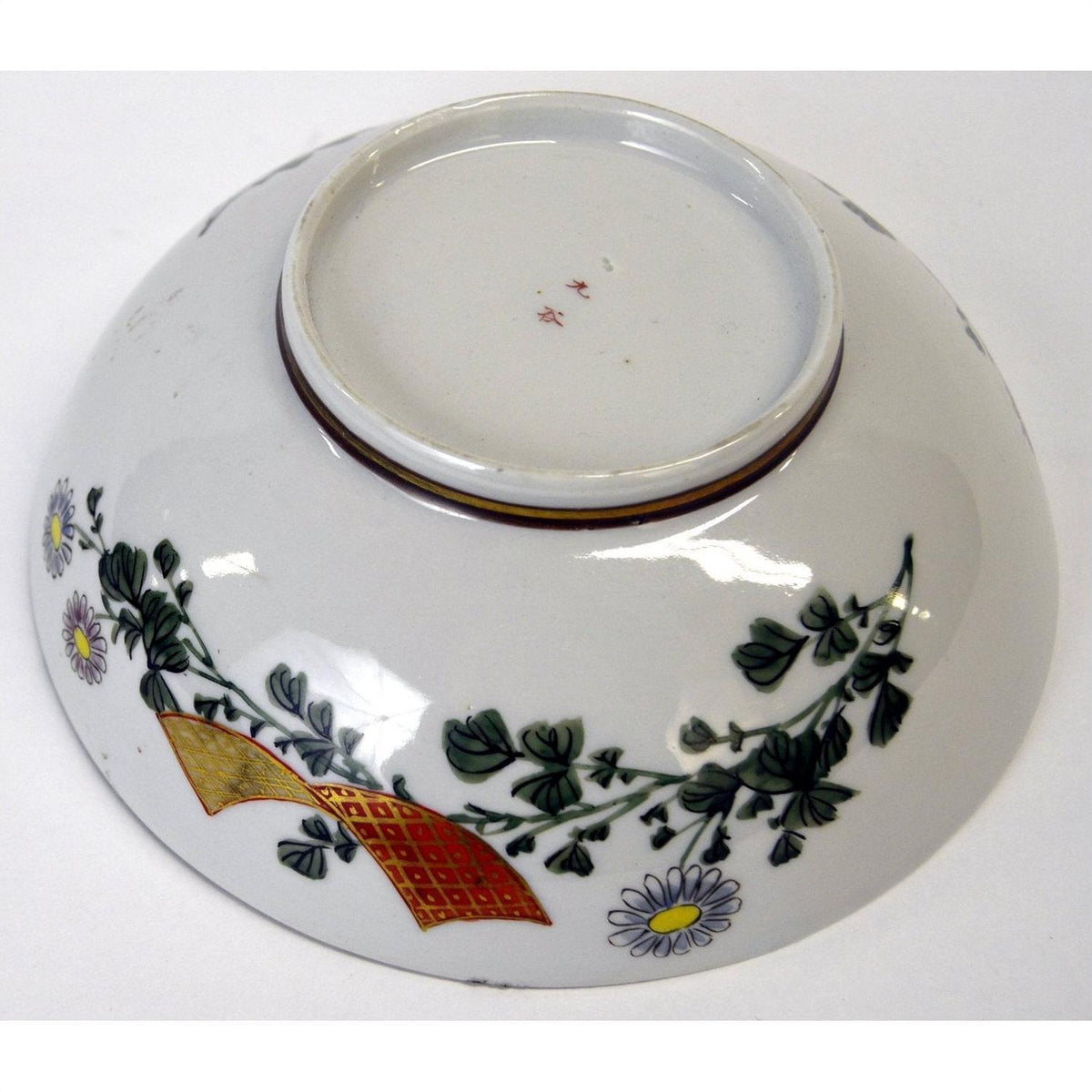 White porcelain bowl with hand painted floral and gold ribbon designs, upside down on white background, 7 inch diameter.