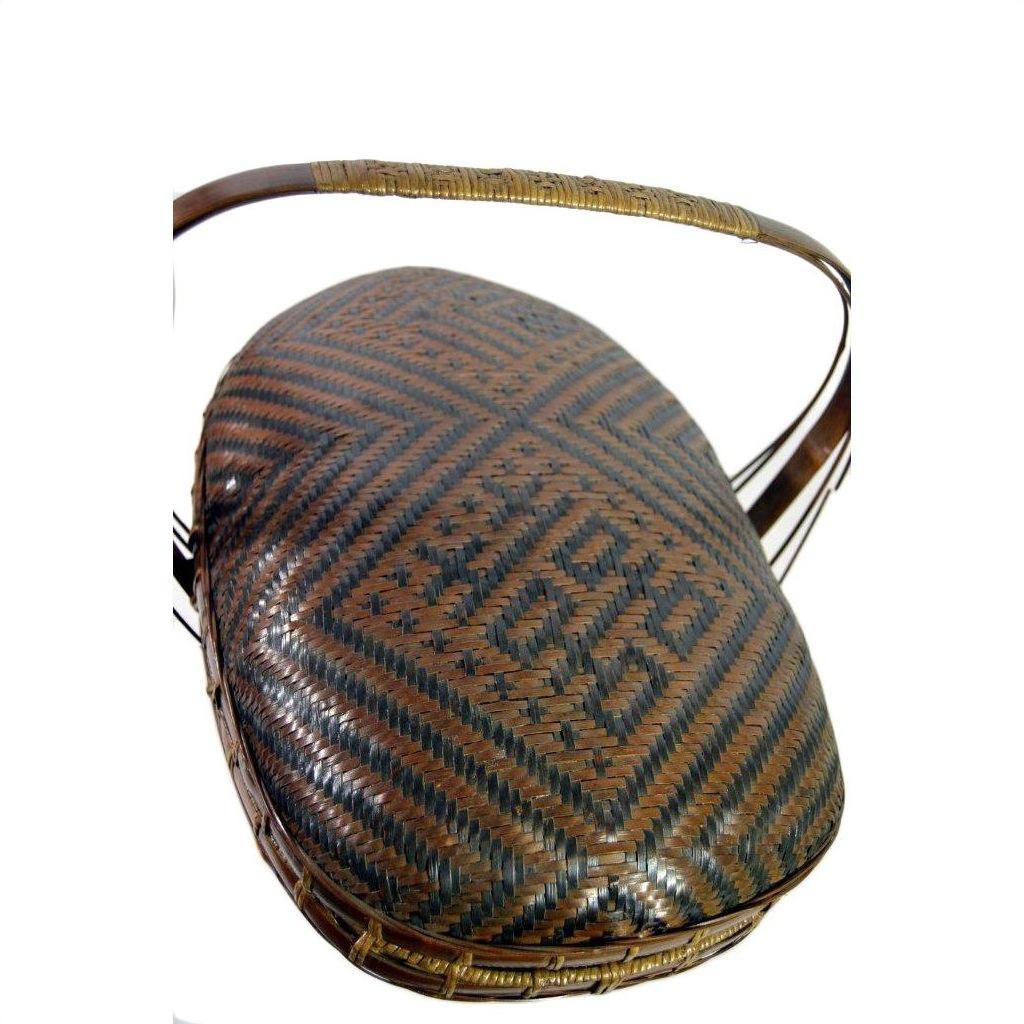 Brown-black rattan basket with curved handle and geometric diamond pattern, close-up on neutral background.