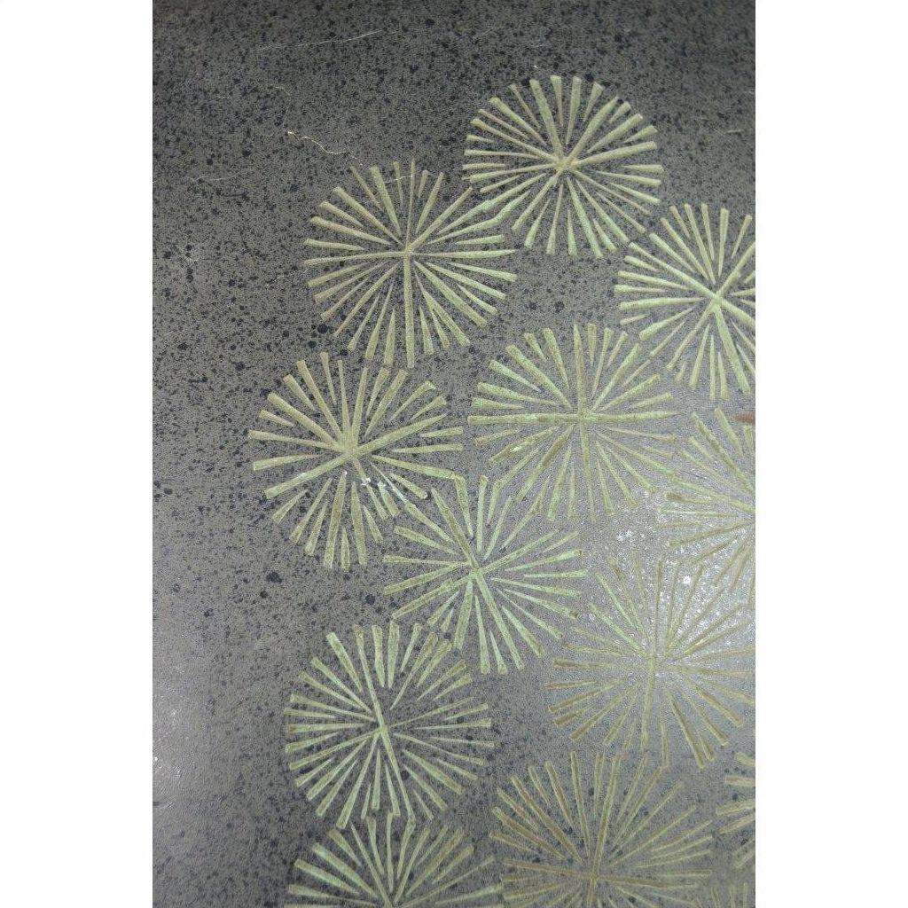 Green ceramic vase with dark speckles and green radial line patterns, abstract flower design, indoors.